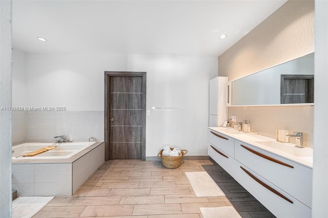 full bath with double vanity, wood tiled floor, a garden tub, and a sink