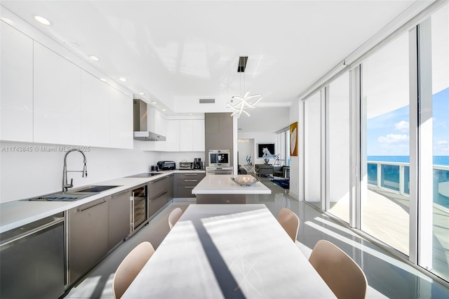 kitchen with wine cooler, light countertops, a sink, modern cabinets, and wall chimney exhaust hood