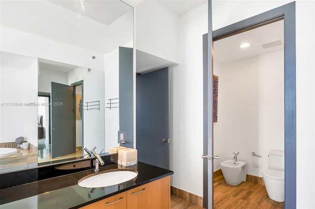 full bathroom featuring baseboards, toilet, wood finished floors, vanity, and a bidet