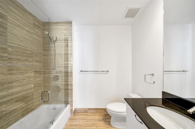 full bath with enclosed tub / shower combo, toilet, wood finished floors, vanity, and visible vents