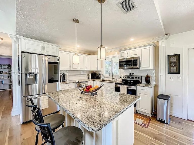 kitchen with a kitchen island, appliances with stainless steel finishes, pendant lighting, sink, and white cabinets