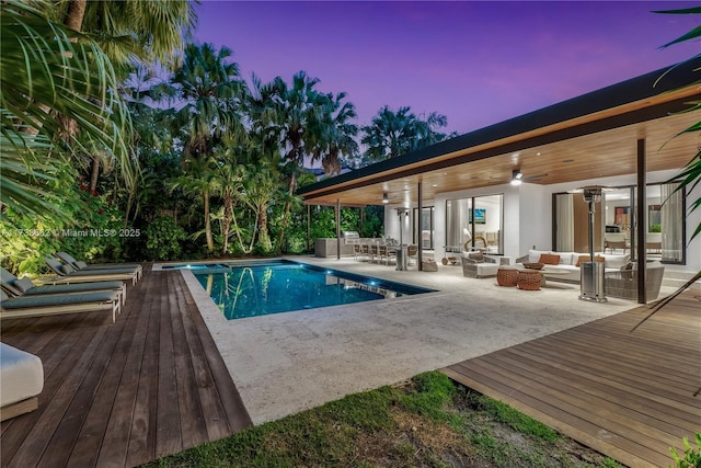 pool at dusk featuring a ceiling fan, an outdoor pool, a wooden deck, and an outdoor hangout area