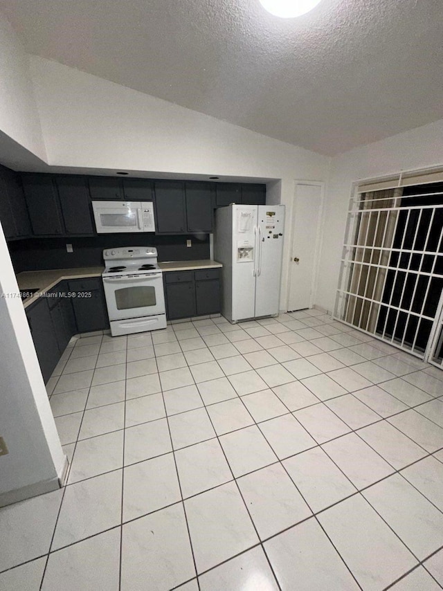 kitchen with light tile patterned flooring, white appliances, vaulted ceiling, and a textured ceiling