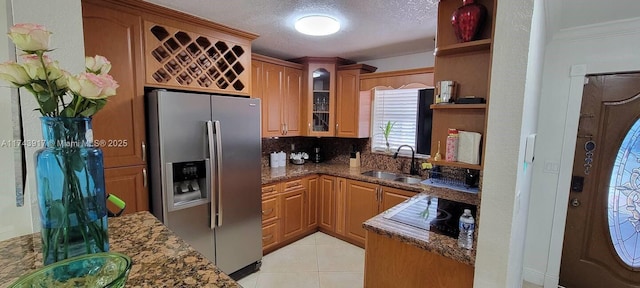 kitchen with sink, dark stone countertops, light tile patterned floors, stainless steel fridge with ice dispenser, and a textured ceiling