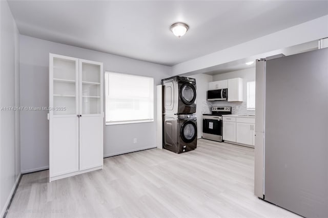 kitchen featuring white cabinetry, backsplash, stacked washer and dryer, stainless steel appliances, and light hardwood / wood-style flooring