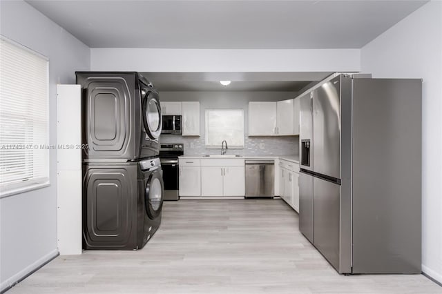 kitchen featuring stacked washer and dryer, sink, stainless steel appliances, white cabinets, and decorative backsplash