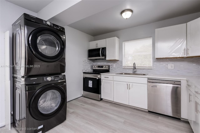 kitchen featuring stainless steel appliances, stacked washer / dryer, sink, and white cabinets