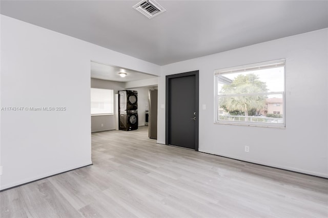 empty room featuring stacked washer and dryer and light hardwood / wood-style flooring