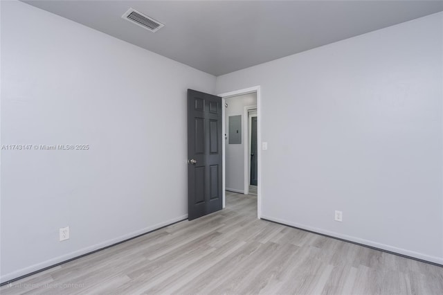 spare room with electric panel and light hardwood / wood-style floors