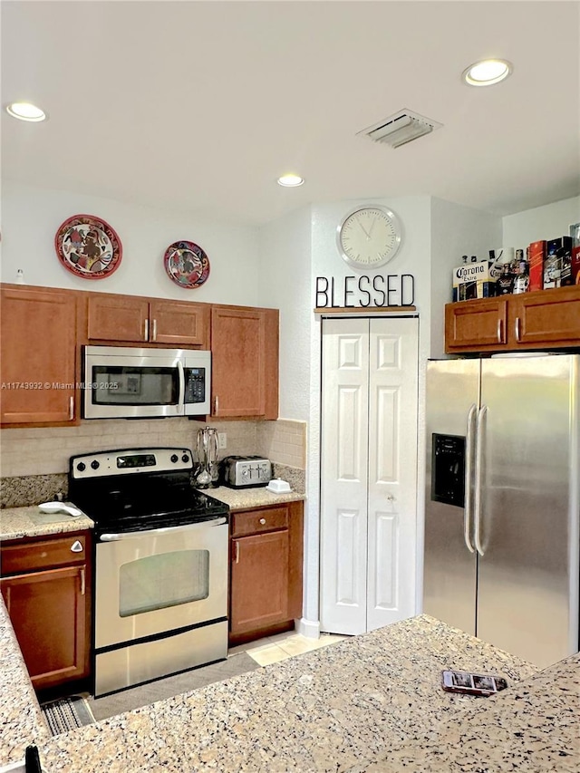 kitchen with decorative backsplash, light stone countertops, and appliances with stainless steel finishes