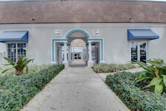 entrance to property featuring french doors, roof with shingles, and stucco siding