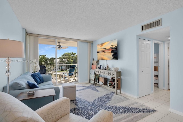 tiled living area featuring a textured ceiling, a ceiling fan, visible vents, baseboards, and expansive windows