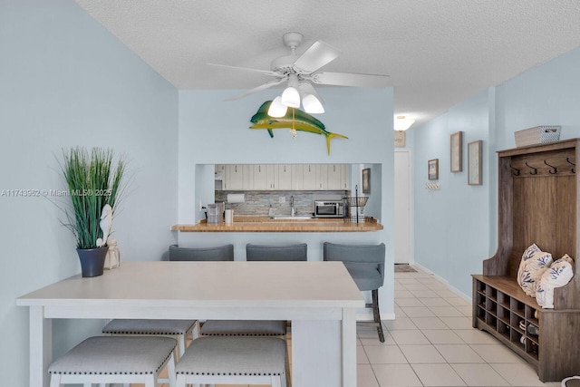 kitchen featuring light tile patterned floors, a peninsula, a ceiling fan, decorative backsplash, and stainless steel microwave