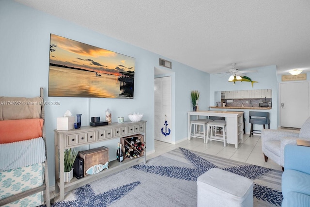 living area with tile patterned flooring, a textured ceiling, visible vents, and a ceiling fan