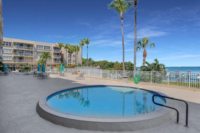 community pool with a water view, fence, and a patio