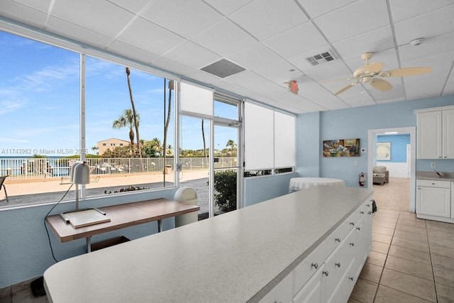 kitchen featuring light tile patterned floors, visible vents, a ceiling fan, white cabinets, and a drop ceiling