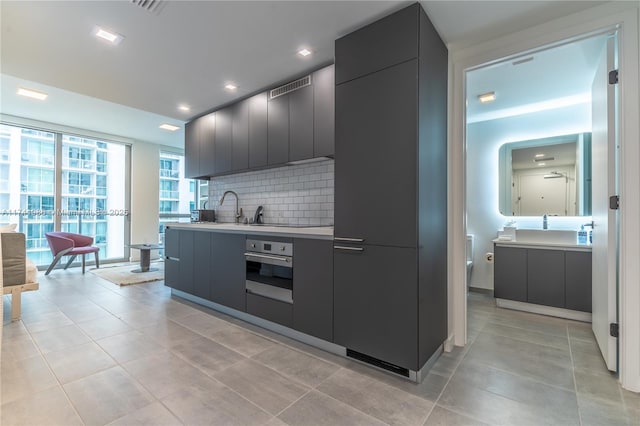 kitchen featuring sink, light tile patterned floors, a wall of windows, decorative backsplash, and oven