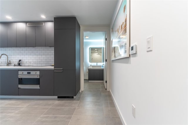 kitchen with gray cabinets, light tile patterned flooring, oven, and backsplash