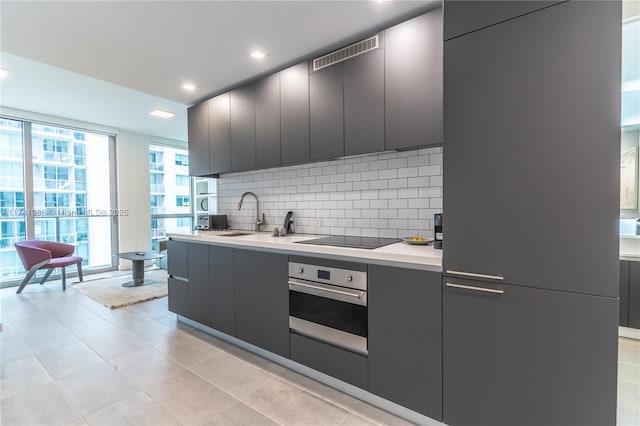 kitchen with light tile patterned flooring, sink, tasteful backsplash, black electric cooktop, and oven