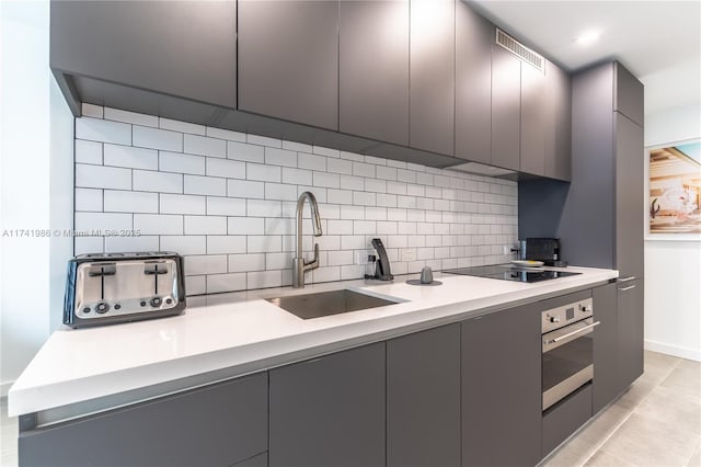 kitchen featuring sink, gray cabinetry, black electric cooktop, decorative backsplash, and oven