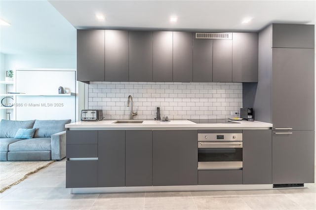 kitchen featuring gray cabinetry, black electric stovetop, decorative backsplash, and stainless steel oven