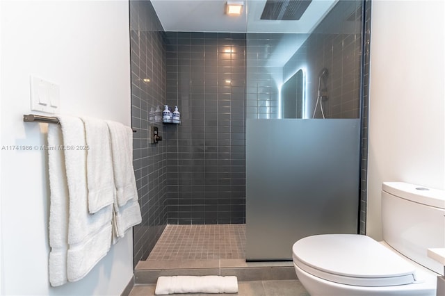 bathroom with tile patterned flooring, a tile shower, and toilet