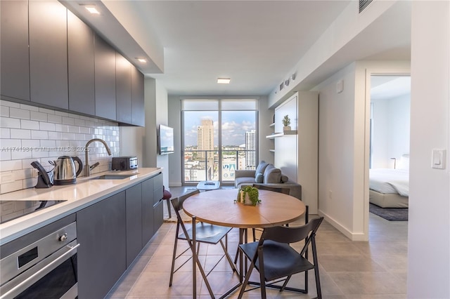 kitchen with sink, backsplash, a wall of windows, stainless steel oven, and black electric cooktop