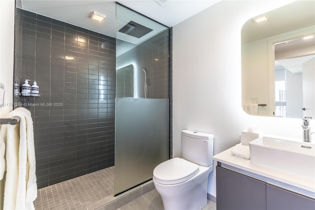 bathroom featuring tile patterned flooring, vanity, a tile shower, and toilet