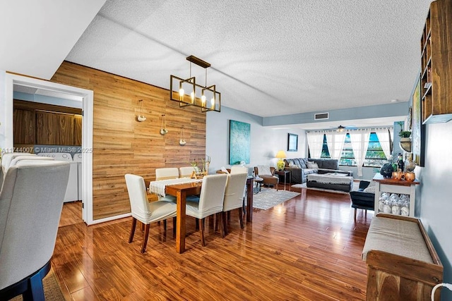 dining area with lofted ceiling, wood-type flooring, a chandelier, a textured ceiling, and wooden walls