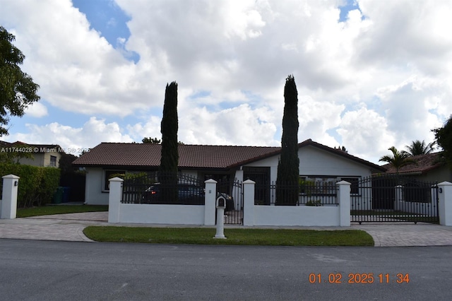 ranch-style house featuring a fenced front yard, a tiled roof, decorative driveway, a gate, and stucco siding