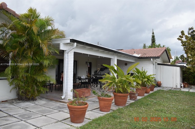 back of house featuring a tiled roof, brick siding, a lawn, and a patio area