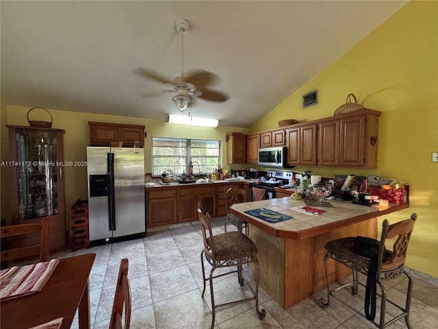 kitchen featuring a breakfast bar area, ceiling fan, stainless steel appliances, tile counters, and kitchen peninsula