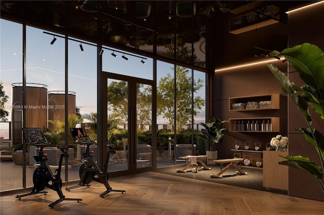 exercise room featuring parquet flooring, a wall of windows, and a towering ceiling