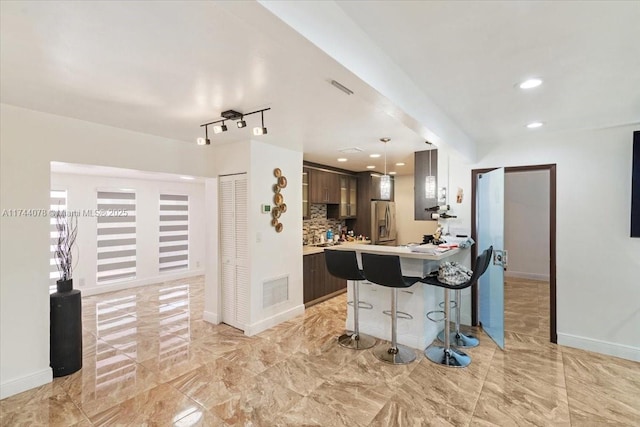 kitchen with a kitchen bar, dark brown cabinets, stainless steel fridge, kitchen peninsula, and decorative backsplash