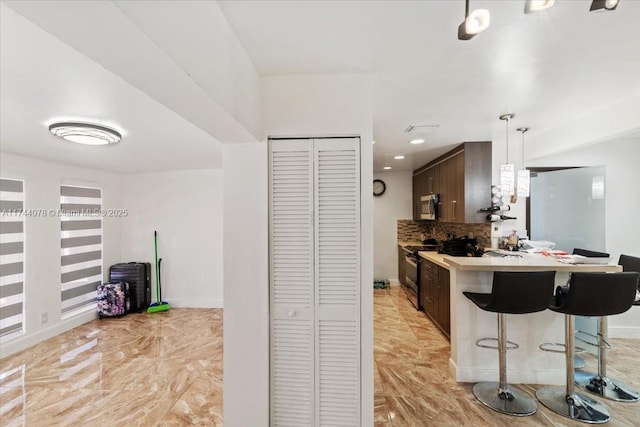 kitchen featuring decorative light fixtures, tasteful backsplash, a breakfast bar area, kitchen peninsula, and dark brown cabinets