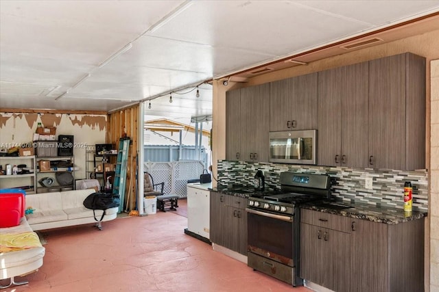 kitchen with stainless steel appliances, backsplash, dark brown cabinetry, and dark stone counters