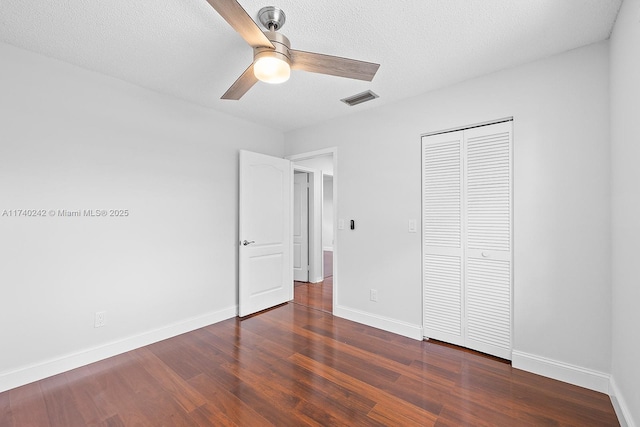 unfurnished bedroom featuring ceiling fan, a closet, dark hardwood / wood-style flooring, and a textured ceiling