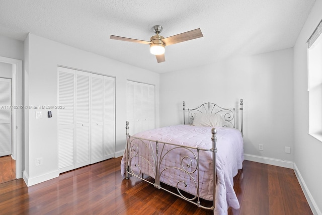 bedroom featuring dark hardwood / wood-style flooring, multiple closets, a textured ceiling, and ceiling fan