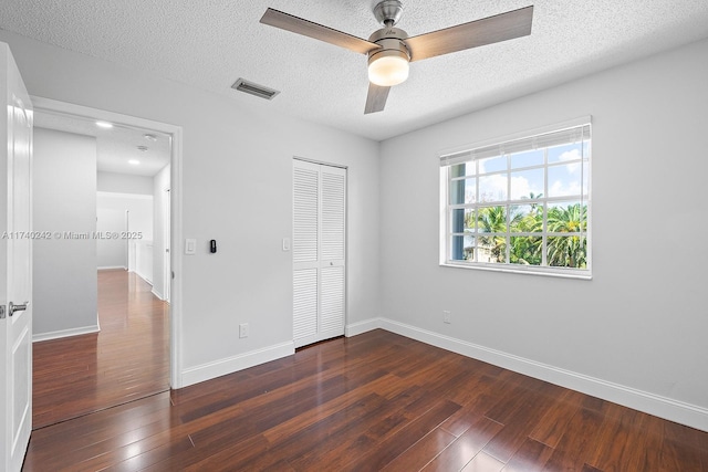 unfurnished bedroom with ceiling fan, a closet, dark wood-type flooring, and a textured ceiling