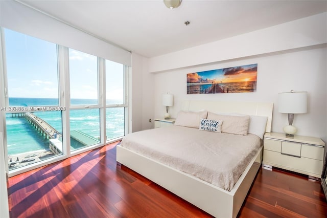 bedroom with a water view, dark wood-type flooring, and access to exterior