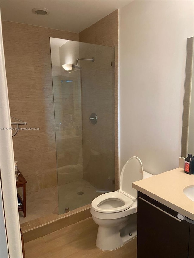 bathroom with hardwood / wood-style flooring, vanity, tiled shower, and toilet