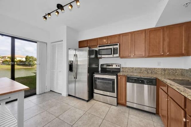 kitchen with appliances with stainless steel finishes, light tile patterned floors, and stone counters