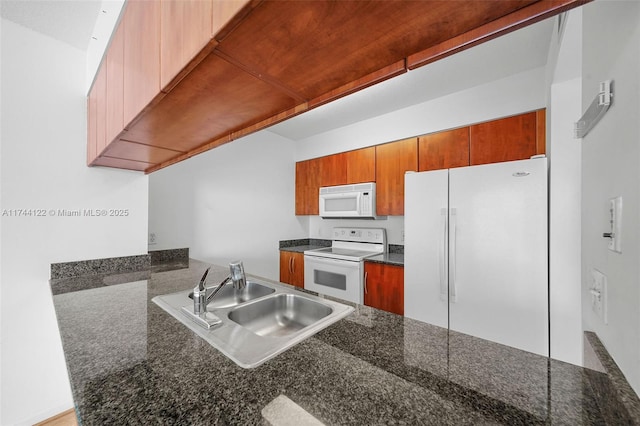 kitchen with sink, white appliances, dark stone counters, and kitchen peninsula