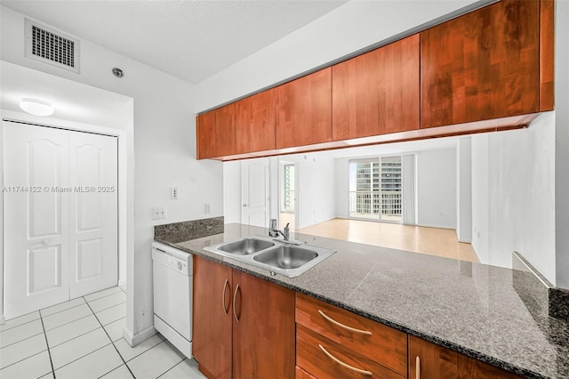 kitchen with light tile patterned floors, white dishwasher, dark stone counters, and sink