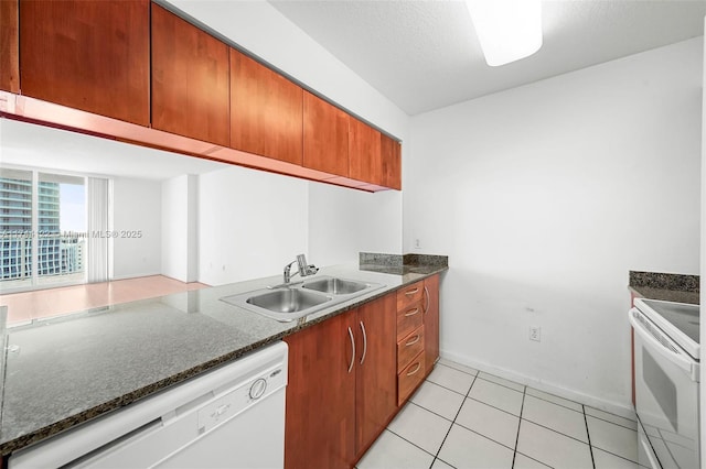 kitchen featuring sink, white appliances, a textured ceiling, light tile patterned floors, and dark stone counters