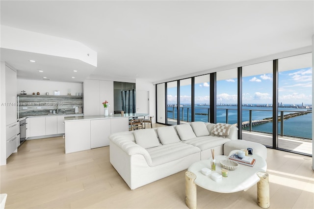 living area featuring a water view, light wood-style floors, a wall of windows, and recessed lighting