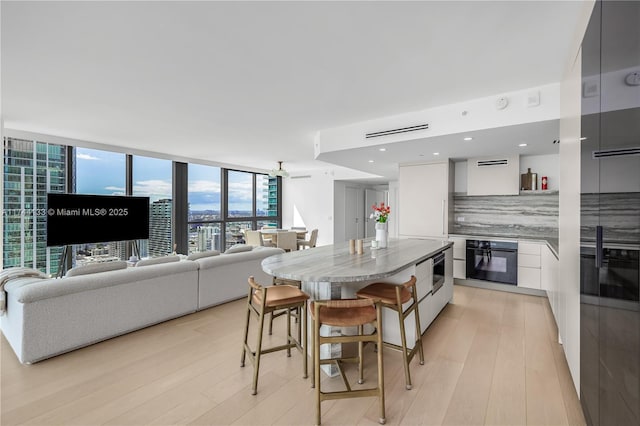 kitchen with light wood-style flooring, white cabinets, black oven, decorative backsplash, and modern cabinets