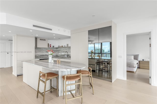 kitchen featuring a breakfast bar, modern cabinets, backsplash, white cabinets, and light stone countertops