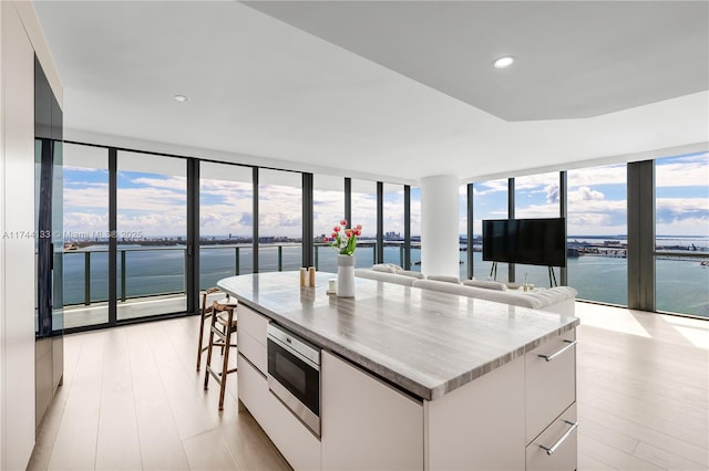 kitchen featuring light wood-style flooring, stainless steel microwave, a water view, expansive windows, and white cabinetry