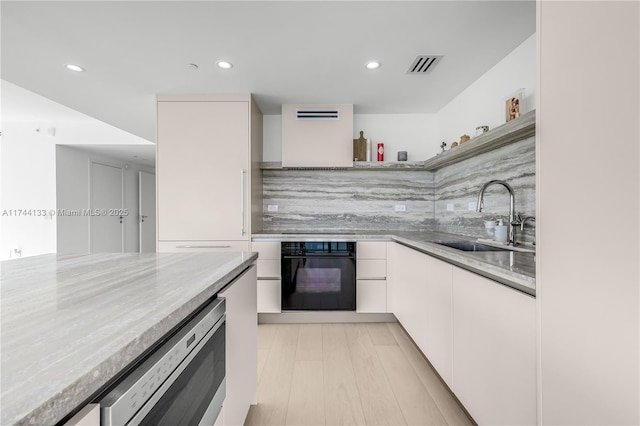 kitchen featuring visible vents, white cabinets, a sink, modern cabinets, and black oven